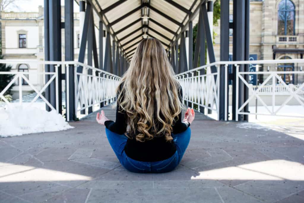 Frau meditiert vor einer Brücke.