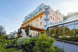 Modernes Klinikgebaeude mit Balkon und Glasfassade, umgeben von Gruen.