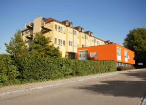 Außenaufnahme von Klinikgebaeude, umgeben von gruenem Gebuesch